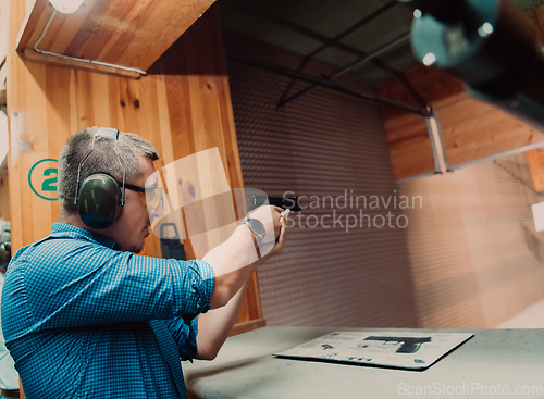 Image of A man practices shooting a pistol in a shooting range while wearing protective headphones
