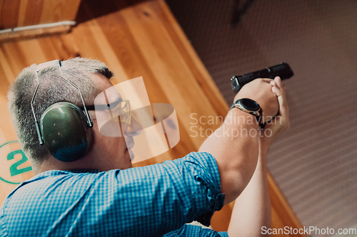 Image of A man practices shooting a pistol in a shooting range while wearing protective headphones