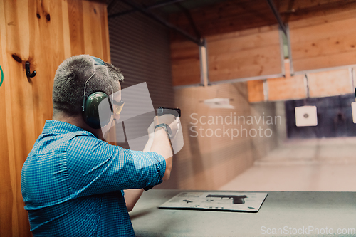 Image of A man practices shooting a pistol in a shooting range while wearing protective headphones