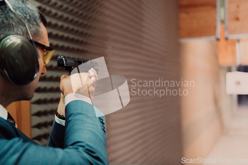 Image of A man practices shooting a pistol in a shooting range while wearing protective headphones