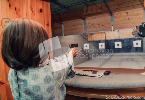 Image of A woman practices shooting a pistol in a shooting range while wearing protective headphones