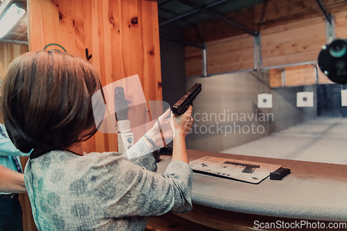 Image of A woman practices shooting a pistol in a shooting range while wearing protective headphones