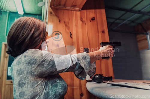 Image of A woman practices shooting a pistol in a shooting range while wearing protective headphones