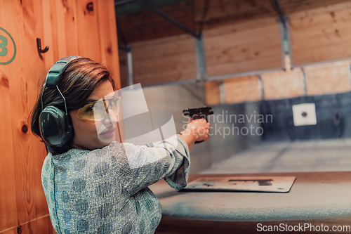 Image of A woman practices shooting a pistol in a shooting range while wearing protective headphones