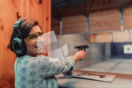 Image of A woman practices shooting a pistol in a shooting range while wearing protective headphones