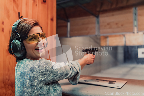 Image of A woman practices shooting a pistol in a shooting range while wearing protective headphones