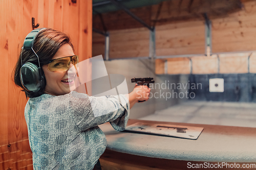 Image of A woman practices shooting a pistol in a shooting range while wearing protective headphones