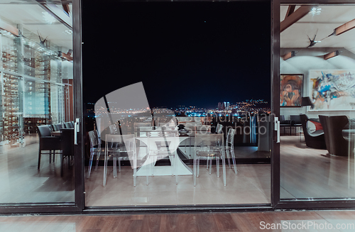 Image of A beautiful house with a beautiful view of the night city. Luxury living room and tereasa with a view of the city. Night photo of a luxury house