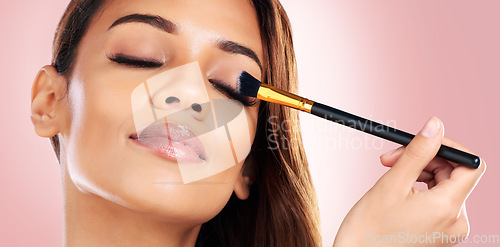 Image of Beauty, eyeshadow and face of woman with makeup brush on pink background for salon, wellness and luxury. Cosmetology, aesthetic and female person with tools for foundation, cosmetics and glamour