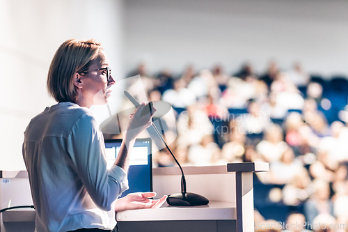 Image of Female speaker giving a talk on corporate business conference. Unrecognizable people in audience at conference hall. Business and Entrepreneurship event.