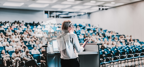 Image of Female speaker giving a talk on corporate business conference. Unrecognizable people in audience at conference hall. Business and Entrepreneurship event.