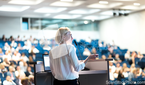 Image of Female speaker giving a talk on corporate business conference. Unrecognizable people in audience at conference hall. Business and Entrepreneurship event.