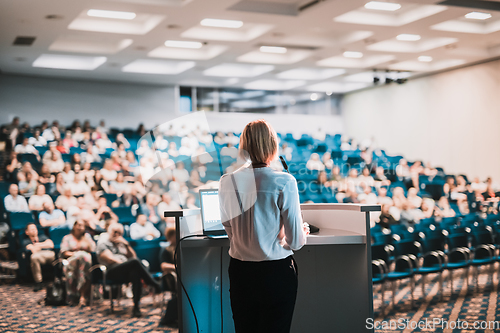 Image of Female speaker giving a talk on corporate business conference. Unrecognizable people in audience at conference hall. Business and Entrepreneurship event.