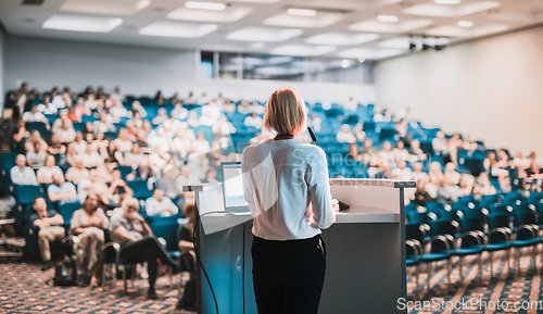 Image of Female speaker giving a talk on corporate business conference. Unrecognizable people in audience at conference hall. Business and Entrepreneurship event.