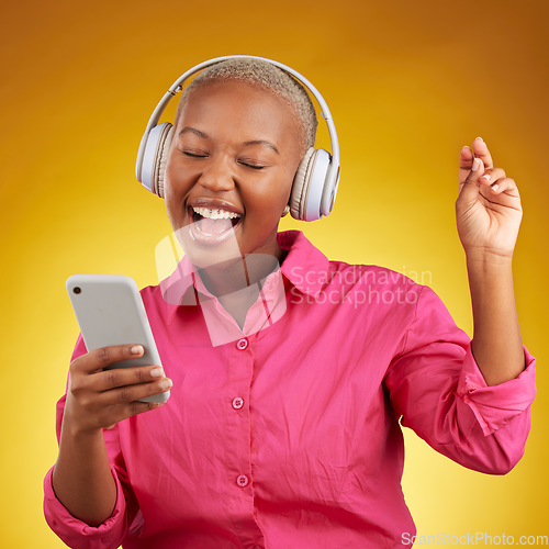 Image of Phone, headphones for music and black woman singing along to radio, sound or podcast in studio isolated on a yellow background. Happy, audio and African person listen, streaming and dance with energy