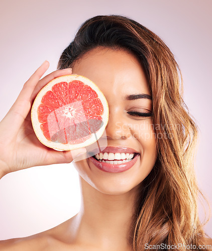 Image of Citrus, grapefruit and face of woman with healthy, natural or organic beauty isolated in a brown studio background. Excited, eyes and young female person with vitamin c for skincare or detox