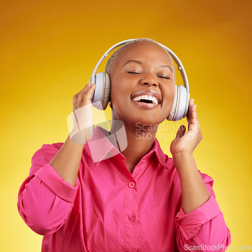 Image of Music headphones, happy and black woman singing in studio isolated on a yellow background. African person, smile and listening to radio, jazz and streaming audio, podcast and hearing sound of hip hop