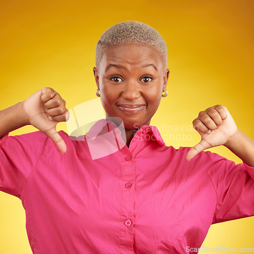 Image of Thumbs down, portrait and black woman in studio with no, bad or negative feedback on yellow background. Face, hands and African female with emoji finger for refuse, deny or vote, fail or wrong choice