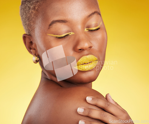 Image of Creative, makeup and woman in a studio with cosmetic eyeliner and lipstick for cosmetology. Self care, glamour and young African female model with a colorful face routine by a yellow background.