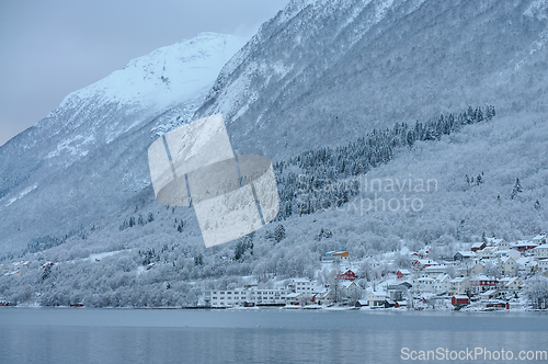 Image of cluster of houses by the sea under snow-covered high mountains
