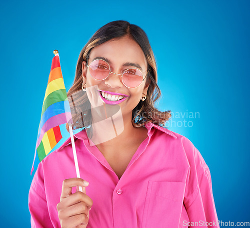 Image of Woman, lgbtq and rainbow flag in studio portrait, sunglasses and sign for pride with human rights by blue background. Gen z girl, young lesbian student and happy with solidarity, freedom or inclusion