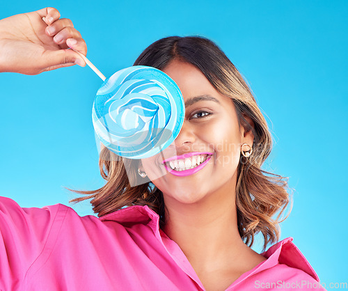 Image of Woman, lollipop eye and studio portrait for eating, sweets and comic smile with food by blue background. Girl, student or young fashion model with candy, beauty and funny with sugar for dessert snack