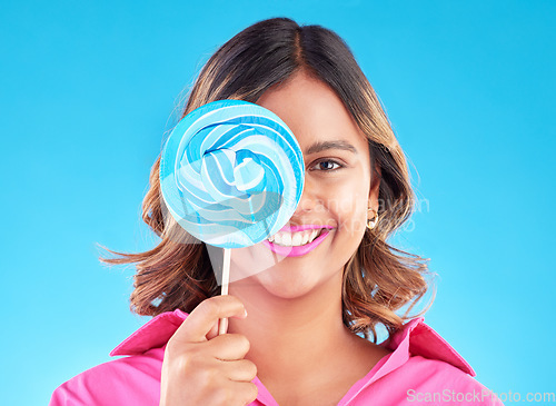 Image of Portrait, lollipop or happy woman on a blue background in studio with positive, sugar or cheerful smile. Colorful sweets, hungry or face of Indian girl eating a giant snack, treats or candy with joy