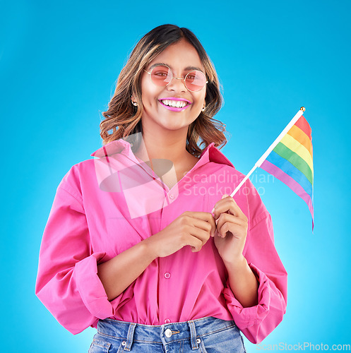 Image of Woman, smile and pride flag in studio portrait with fashion, sunglasses and sign for human rights by blue background. Gen z girl, lesbian student and happy at protest, support and freedom for lgbtq