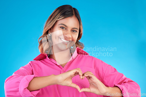 Image of Woman, heart shape and smile portrait in studio for love, fashion or happiness. Happy person show sign with hands, icon or emoji for support, kindness and motivation for charity on a blue background