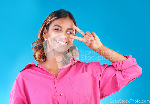 Image of Smile, happy and peace sign with portrait of woman in studio for support, gen z and emoji. Motivation, kindness and winner with face of person on blue background for v icon, positive and symbol