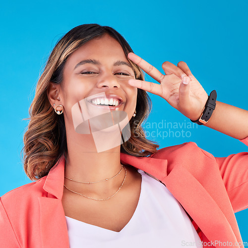 Image of Peace sign, happy and portrait of a woman on a blue background for fashion, comedy and young. Smile, face and an Indian girl or model with a hand gesture for crazy isolated on a studio backdrop