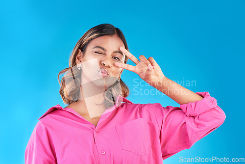Image of Wink, kiss and peace sign with portrait of woman in studio for support, gen z and emoji. Motivation, kindness and winner with face of person on blue background for v icon, positive and symbol