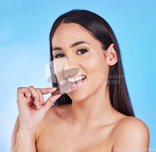 Image of Chocolate, sugar and portrait of woman in studio eating luxury, sweet treats and candy on blue background. Happy, unhealthy diet and face of female person with cocoa bar, dessert and delicious snack