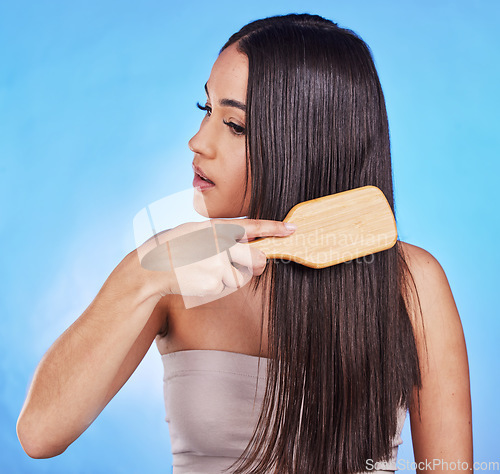 Image of Hair care, beauty and a woman with a brush in studio for self love, hygiene and shine. Salon, hairdresser and a female model person with shampoo, cosmetics and a hairbrush on a blue background