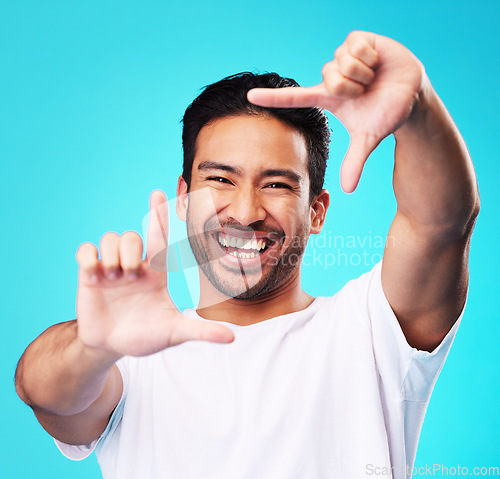 Image of Happy, hand frame and portrait of a man for a selfie, creative aesthetic or advertising photography. Smile, laughing and face of an Asian person with a gesture for a photo on a blue background