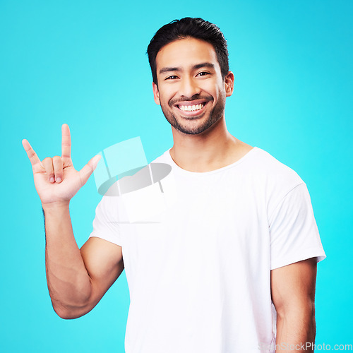 Image of Man, horns and love in studio portrait with smile, kindness and sign language by blue background. Young guy, student and happy with icon, emoji and hand with care, romance or vote with white t-shirt