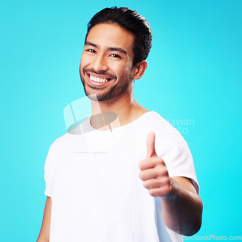 Image of Smile, thumbs up and portrait of a man in a studio with a satisfaction sign or expression. Happy, emoji and young Indian male model with an agreement hand gesture isolated by a blue background.