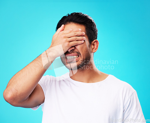 Image of Scared, covering eyes and a man on a blue background for fear, anxiety or angry with a problem. Mental health, fail and a person with hands on face while frustrated and isolated on a studio backdrop