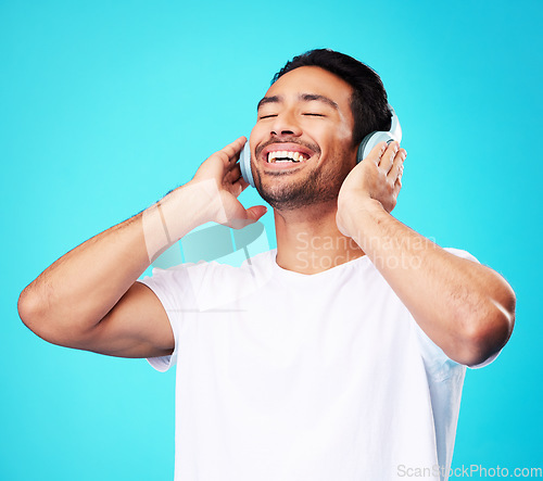 Image of Music, headphones and happy man listening in studio isolated on a blue background. Radio, smile and person with audio, sound or hearing podcast, jazz or media for hip hop with eyes closed for freedom