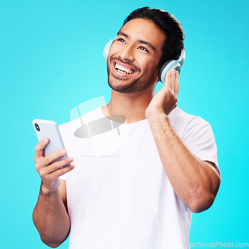 Image of Music, headphones and Asian man with phone for listening in studio isolated on a blue background. Radio, smile and person with audio, sound and hearing podcast, jazz or media for hip hop with mobile