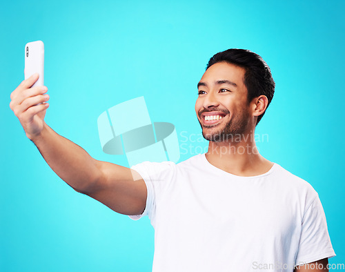 Image of Asian man, selfie and smile in studio for social media post, web chat and excited by blue background. Young guy, student or influencer with memory, profile picture and photography for update on blog