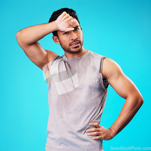 Image of Portrait, fitness and Asian man tired after exercise in studio isolated on a blue background. Face, serious and athlete with fatigue, wipe sweat and workout for sports, healthy body and wellness