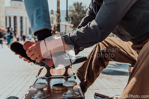 Image of An old man hand polishing and painting a black shoe at street