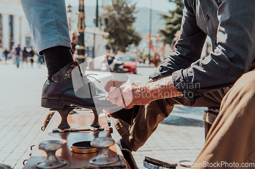 Image of An old man hand polishing and painting a black shoe at street