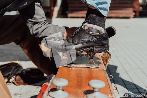 Image of An old man hand polishing and painting a black shoe at street