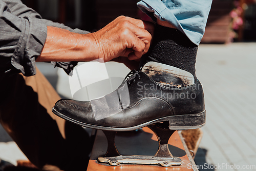 Image of An old man hand polishing and painting a black shoe at street