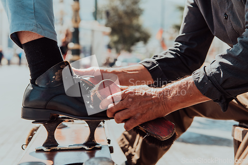 Image of An old man hand polishing and painting a black shoe at street