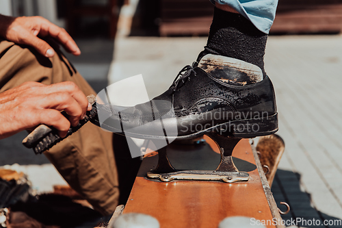 Image of An old man hand polishing and painting a black shoe at street