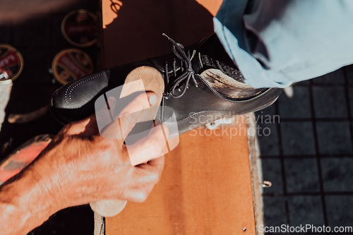 Image of An old man hand polishing and painting a black shoe at street