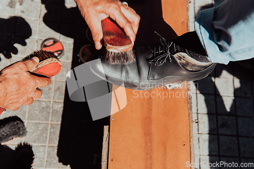 Image of An old man hand polishing and painting a black shoe at street